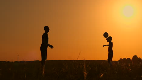 Father-and-son-playing-football-in-the-park-at-sunset-silhouettes-against-the-backdrop-of-a-bright-sun-slow-motion-shooting.